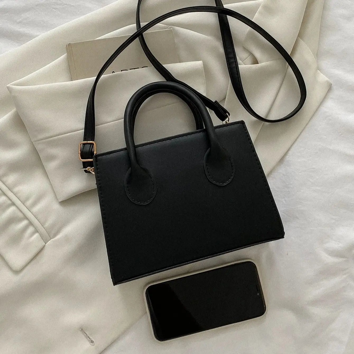 Structured black leather purse displayed next to a smartphone to demonstrate its practical size.