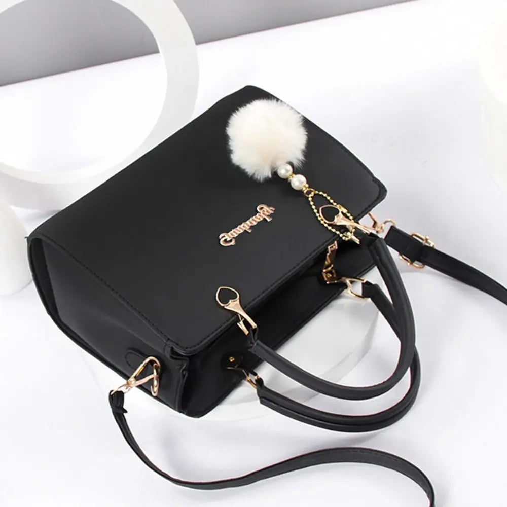 Classic black professional handbag with gold buckles and a white pompom accessory