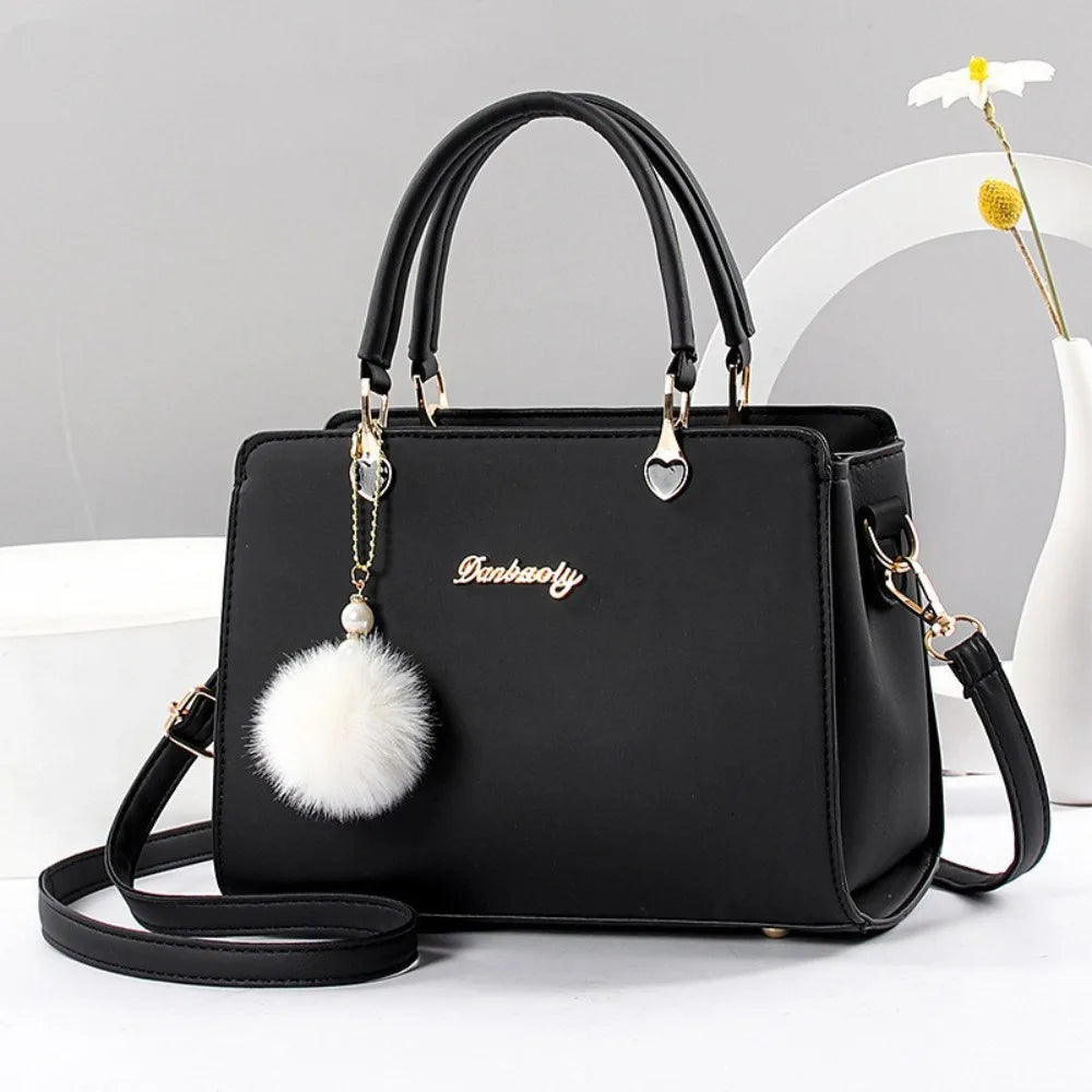 Classic black handbag with gold-tone hardware and a decorative white fluffy pompom charm