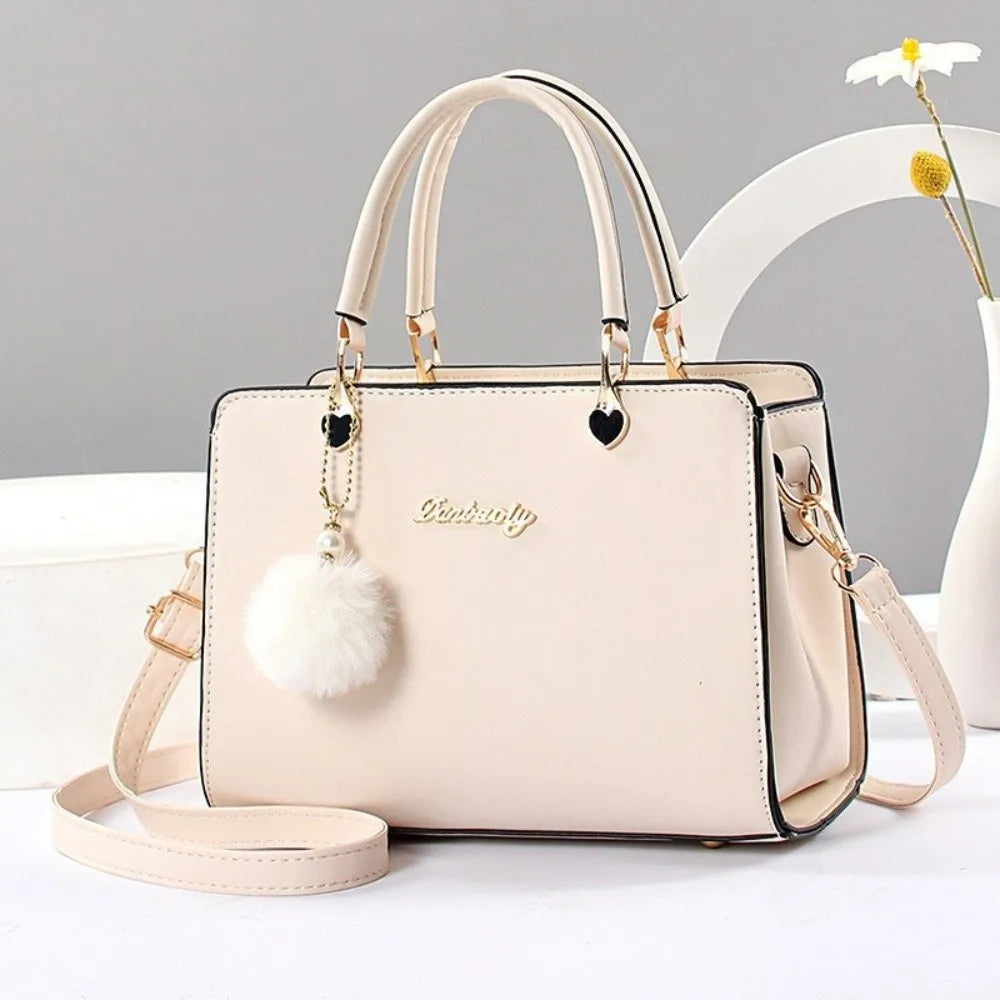 Elegant cream white handbag with gold-tone hardware and a decorative white fluffy pompom charm