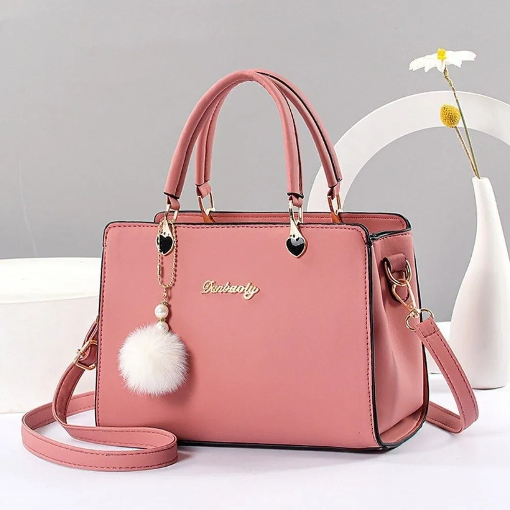 Elegant dusty pink handbag with a classic top handle and decorative white pompom charm