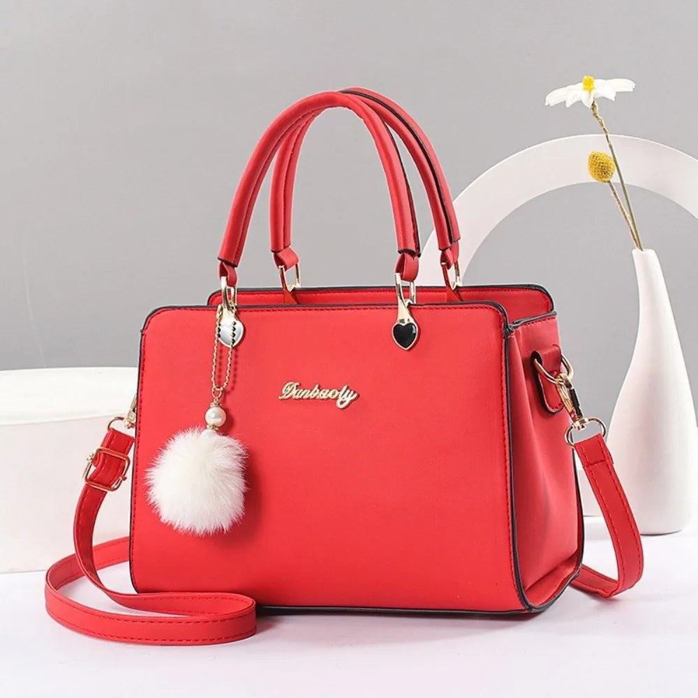 Stylish vibrant orange handbag with elegant gold-tone hardware and a white pompom charm