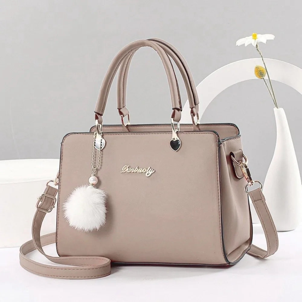 Elegant lilac handbag with top handle, adjustable strap, and white pompom charm