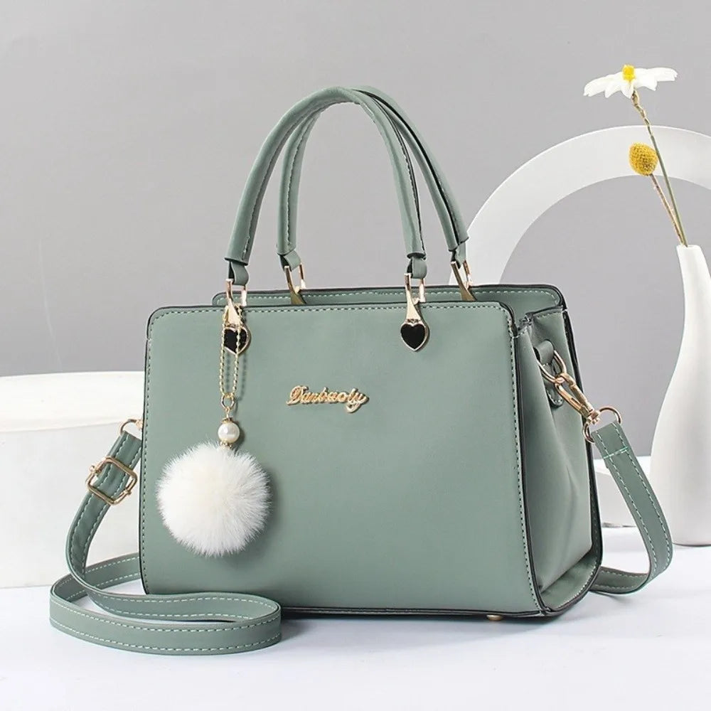 Elegant mint green handbag with gold-tone hardware and a decorative white pompom charm