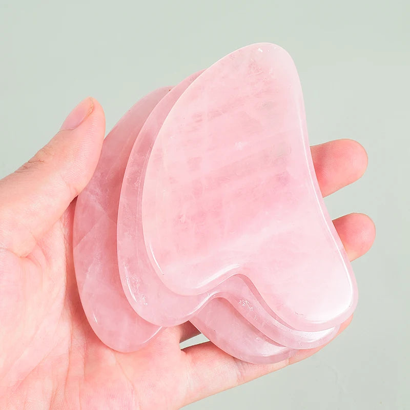 Hand holding multiple heart-shaped pink rose quartz gua sha stones for facial massage - Aurora Nova 4