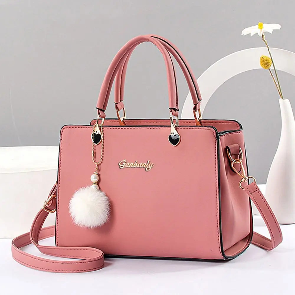 Elegant soft pink handbag with gold-tone hardware and a decorative white fluffy pompom charm