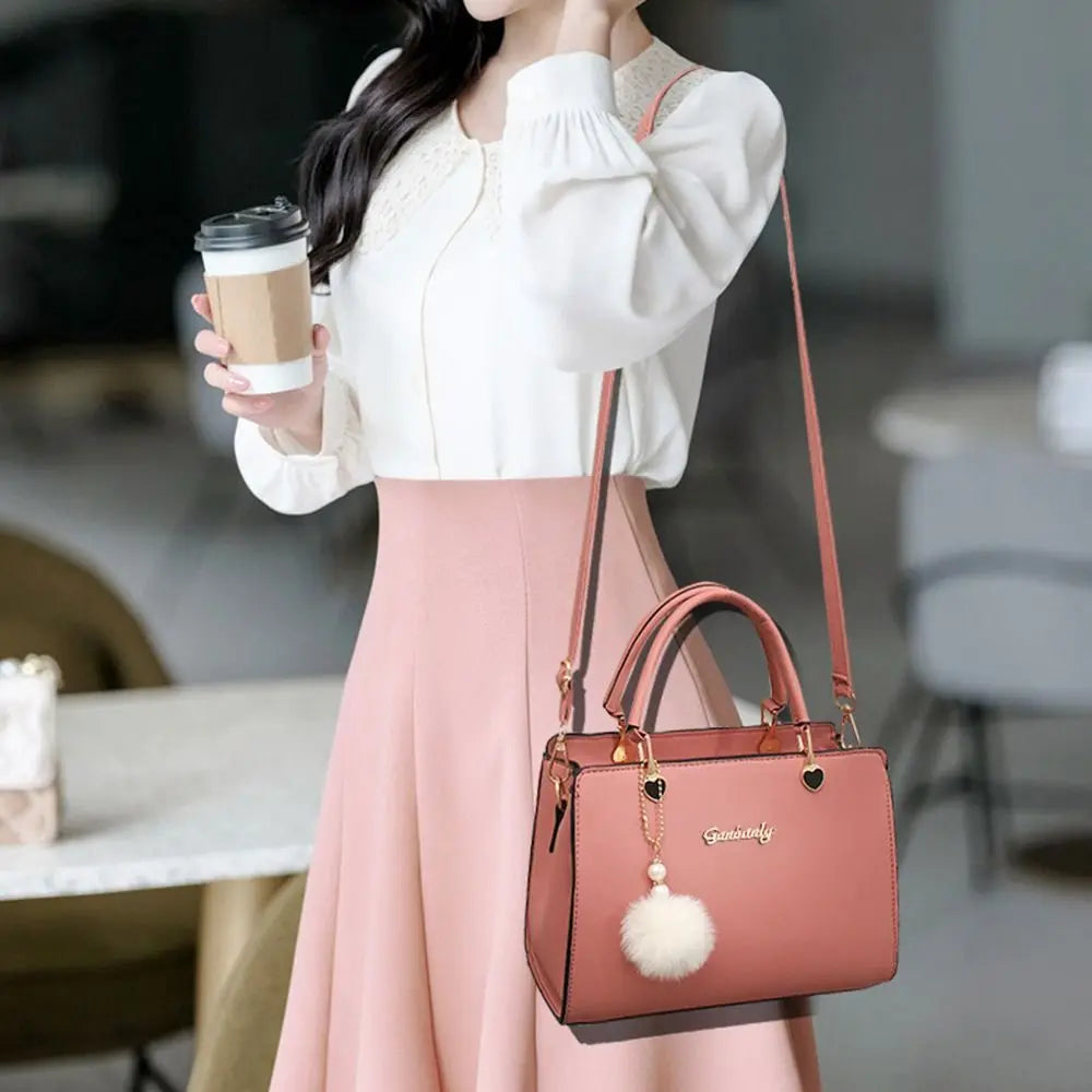 Elegant terracotta brick red handbag with top handle and decorative white pompom, carried by a model
