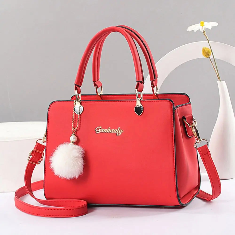 Stylish vibrant orange handbag with a white pompom charm and elegant top handle